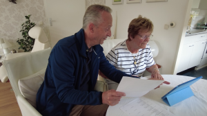 Twee mensen zitten aan de eettafel en nemen samen een bankdocument door, met papieren en een tablet in een rustige thuisomgeving.