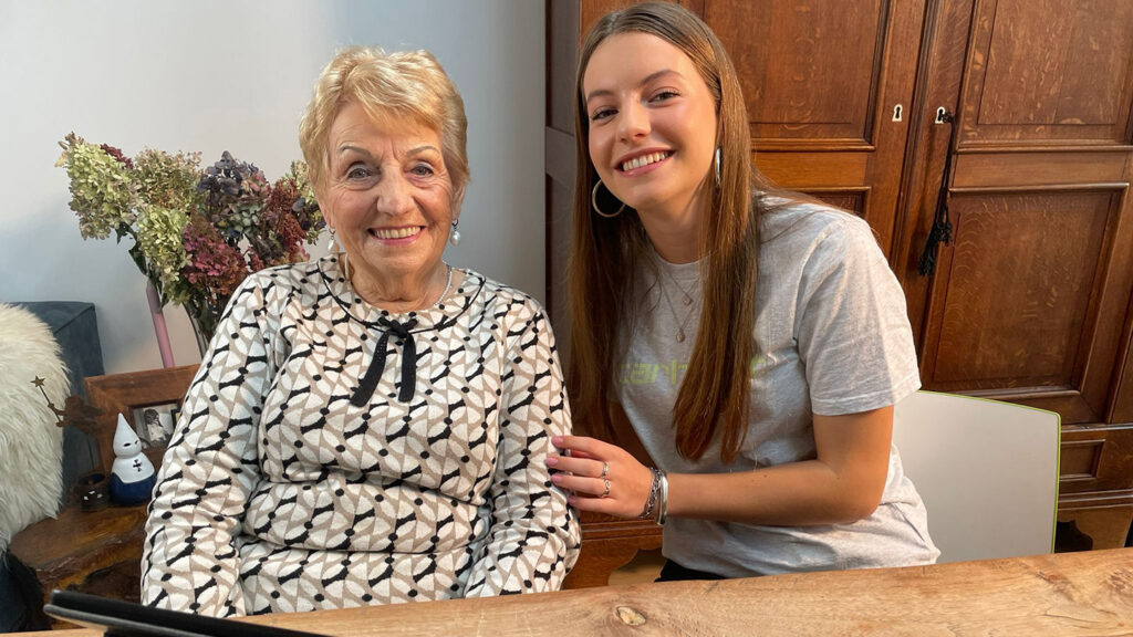 Twee personen zitten samen aan een houten tafel met een tablet en bespreken digitale bankzaken in een huiselijke omgeving.